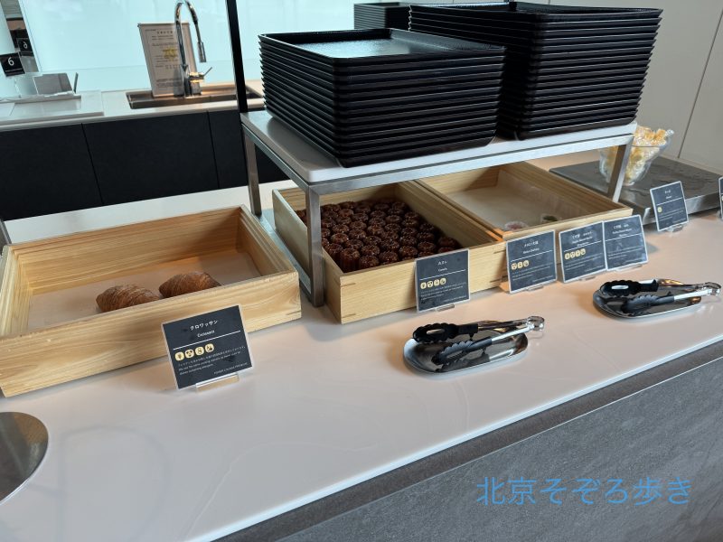 空港ラウンジのビュッフェカウンターに並ぶクロワッサンやカヌレなどの軽食と食器類